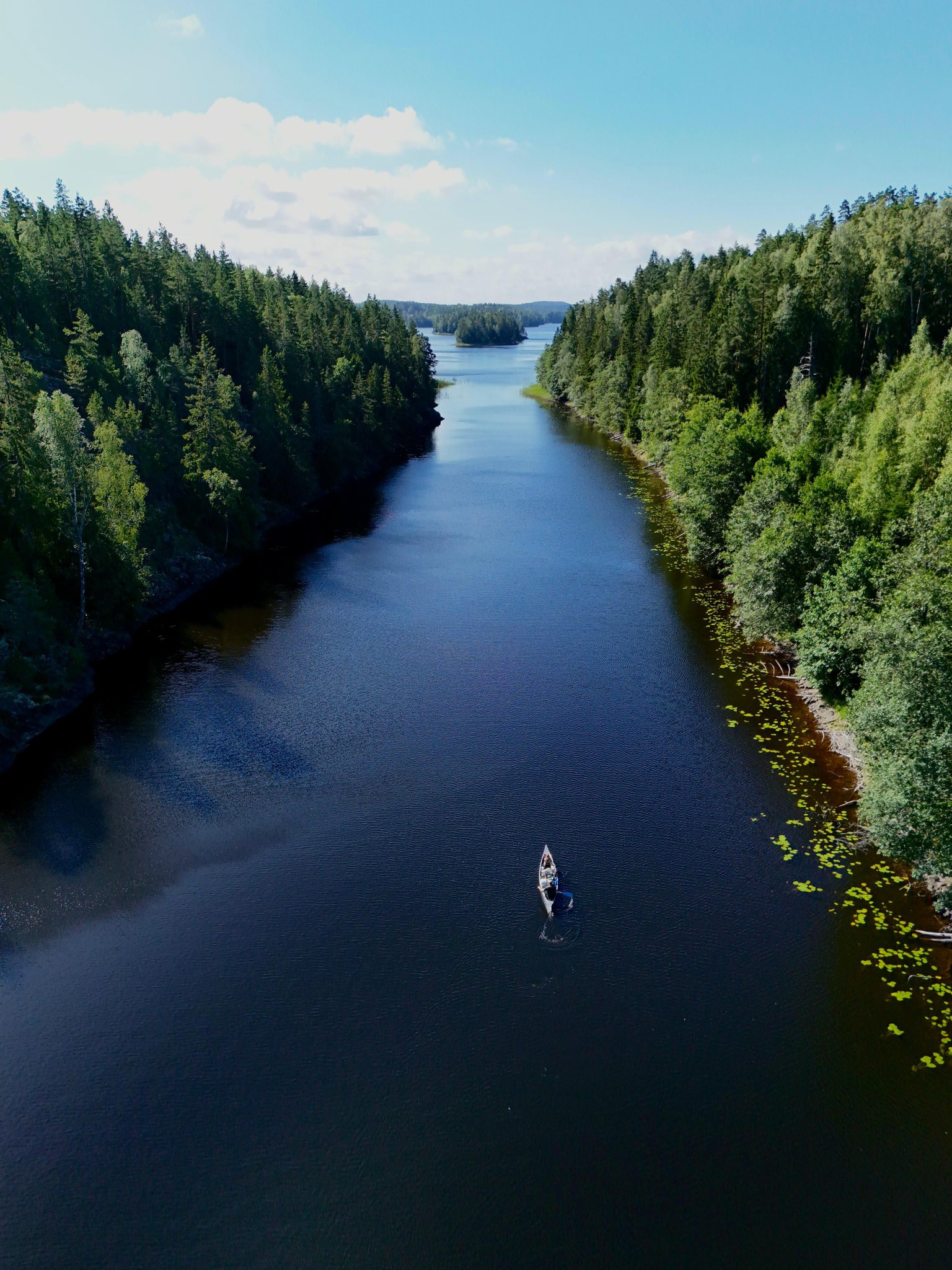 Luchtfoto van een eenzame kanoër op een diepblauw meer omgeven door dichte groene bossen in Zweden.